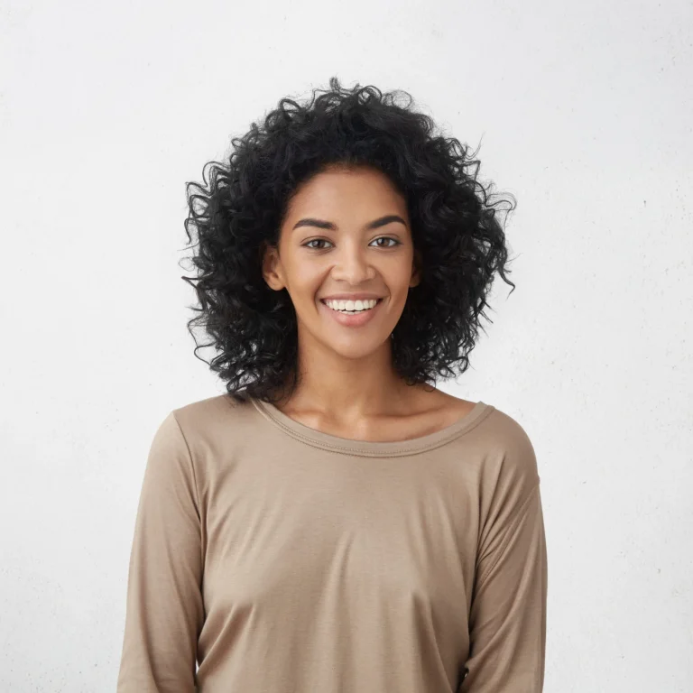 Smiling woman with curly hair wearing a beige top, symbolizing confidence and well-being.