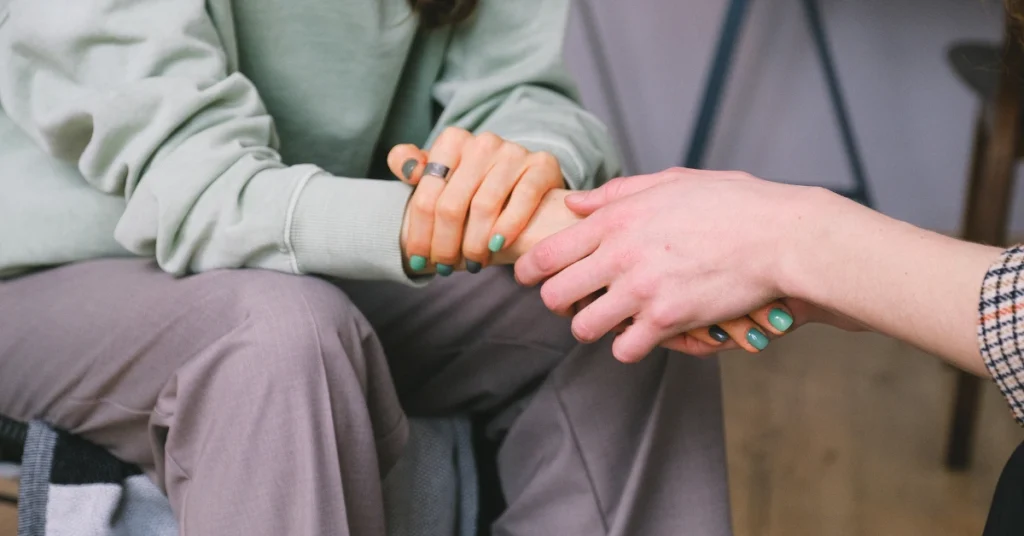 Close-up of two people holding hands in a counseling session, symbolizing emotional support and empathy.