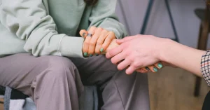 Close-up of two people holding hands in a counseling session, symbolizing emotional support and empathy.